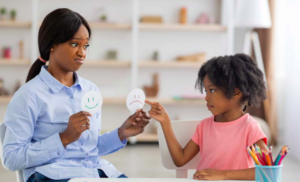 Counselor holds up happy face and sad face images to young patient